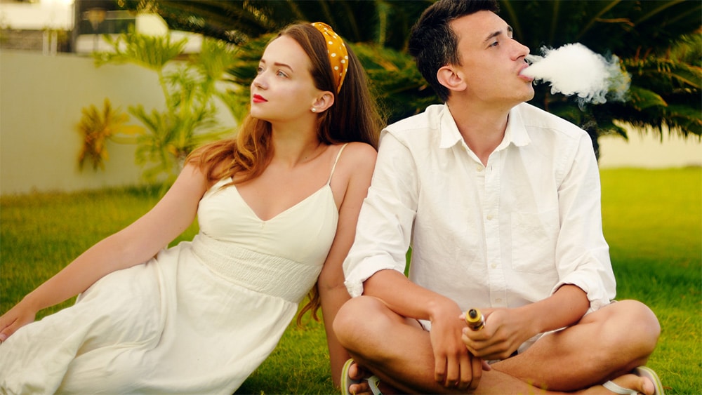 A man and a woman sitting next to one another on green grass using a THCa vape near Stockton, California.