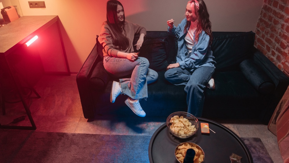 Two women sitting on a couch enjoying Anchorage THCa pre rolls.